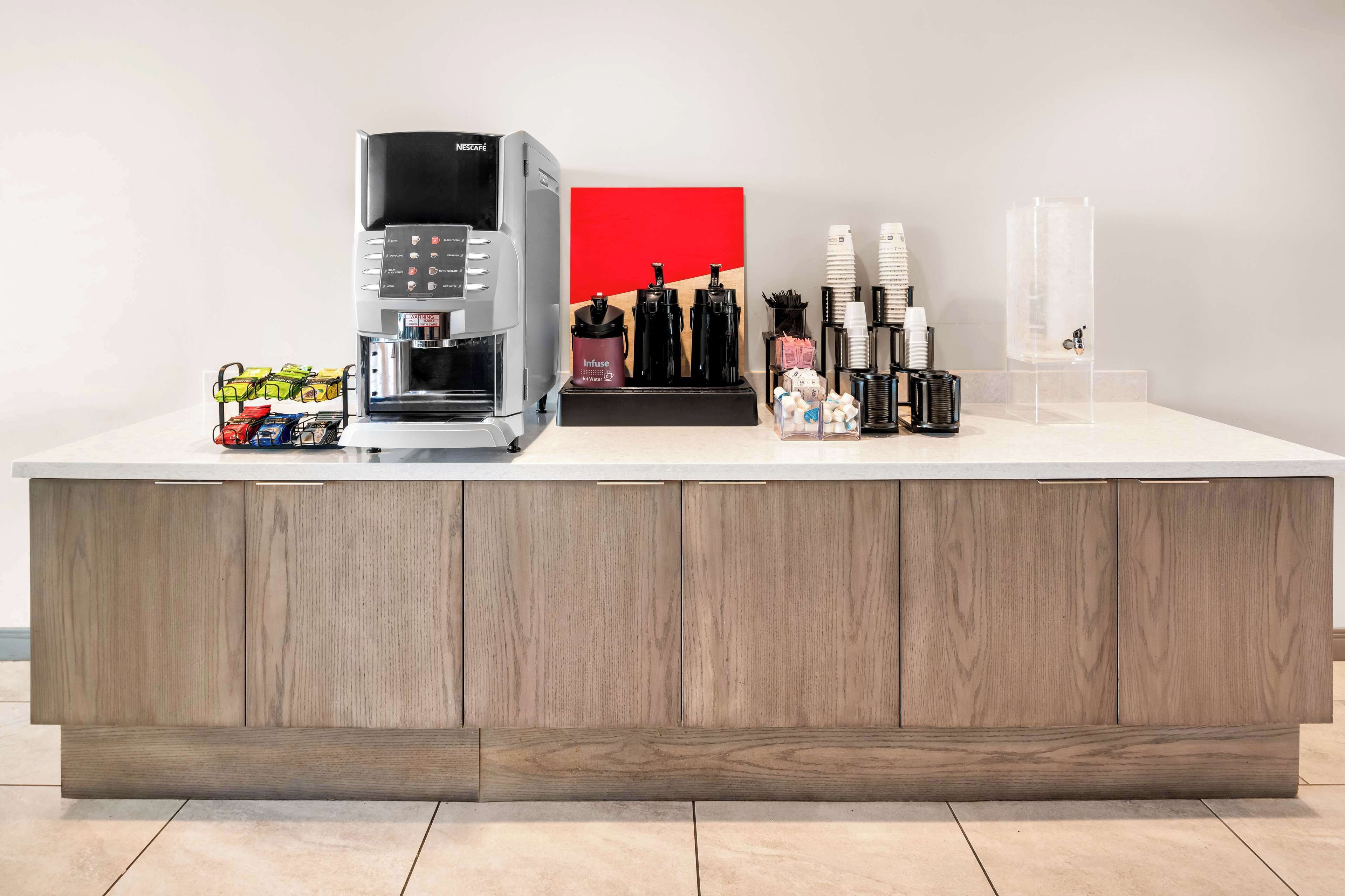 Una estación de café moderna con una máquina de Nescafé, una obra de arte roja y varios accesorios para café.