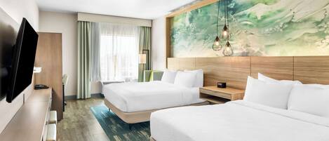 A hotel room with two beds, a flat-screen TV, a wooden desk, and a large abstract painting on the wall.