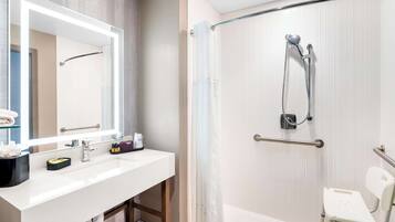 A modern bathroom with a white sink, a large mirror, a shower with a glass door, and a wheelchair-accessible bench.