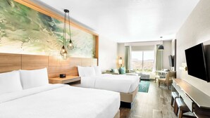 Habitación de hotel con dos camas, un televisor, un escritorio y un ventanal con vistas.