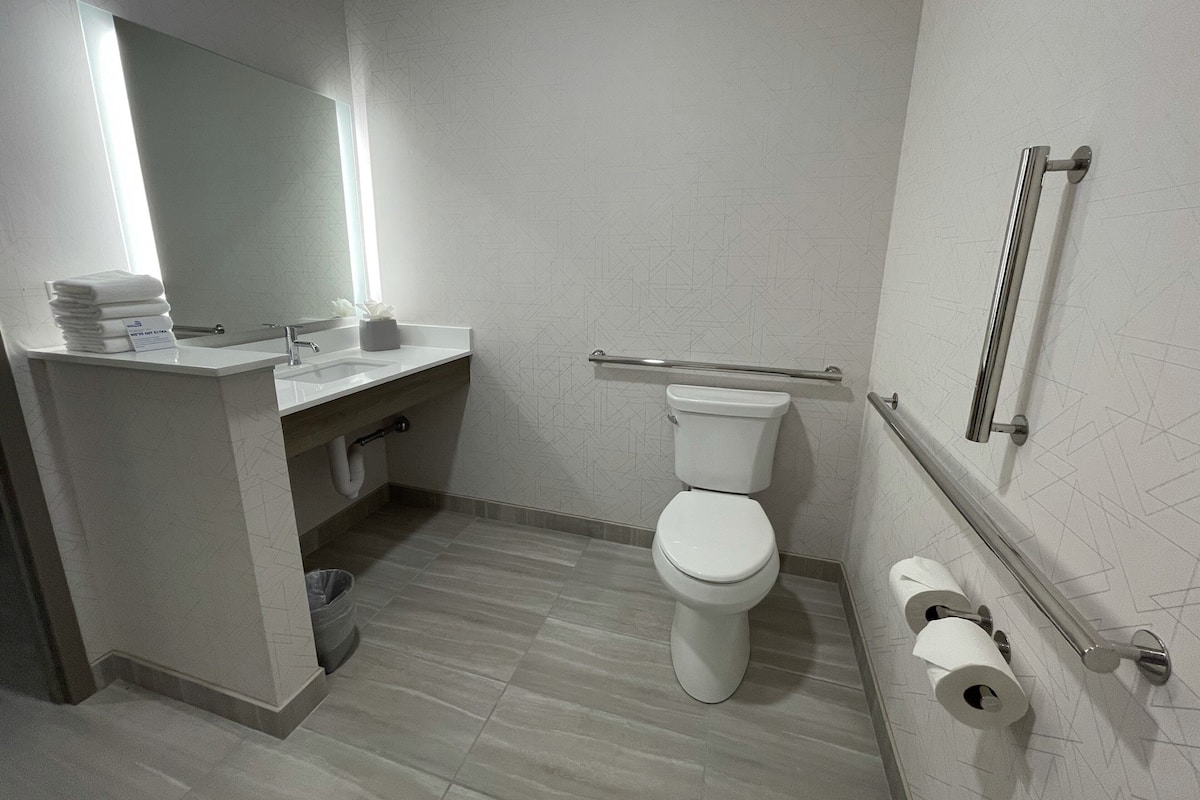 A modern bathroom with a toilet, sink, and handrail.
