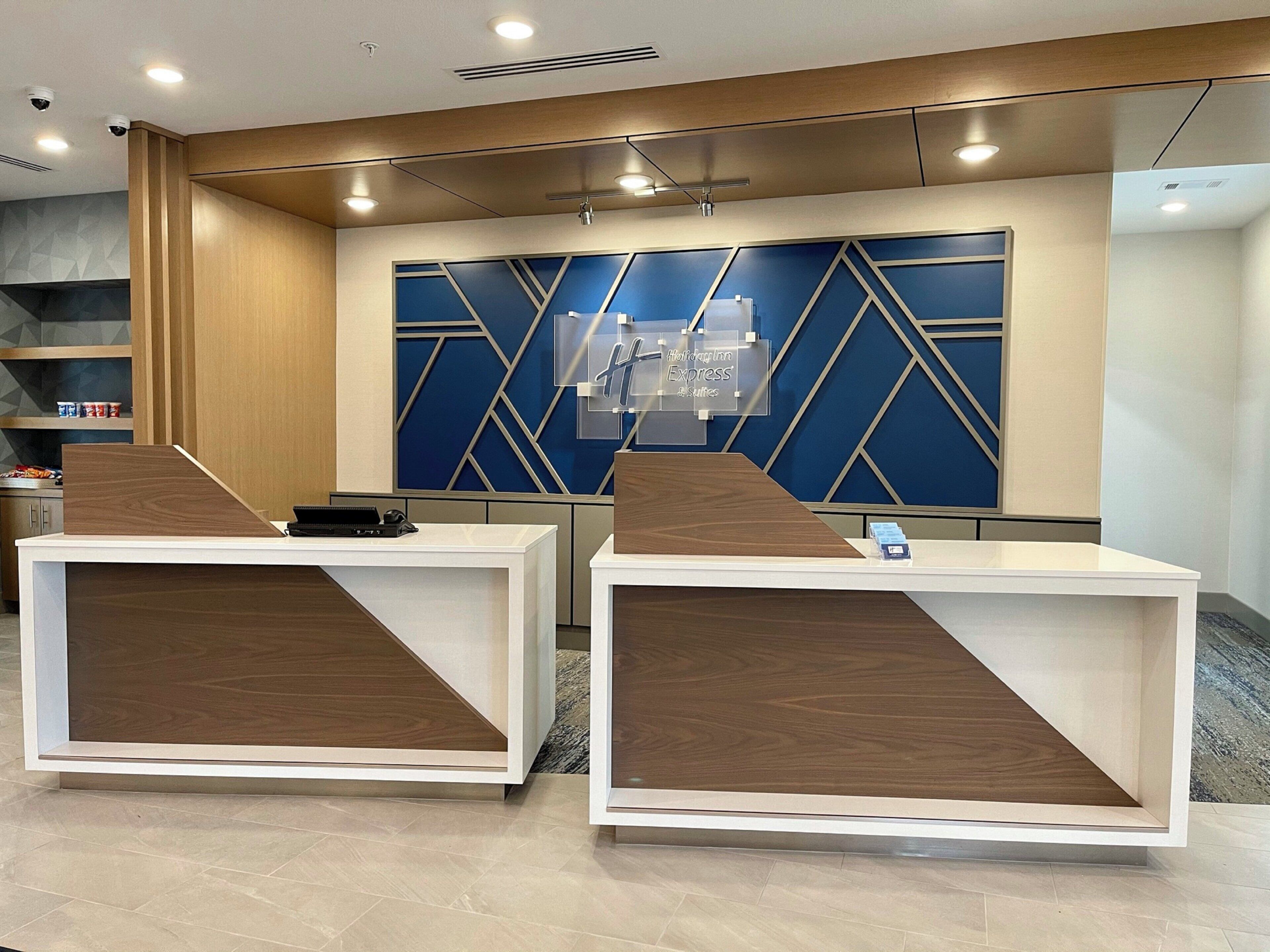 A reception desk area with two counters, a blue geometric wall design, and a ceiling with recessed lighting.