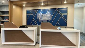 A reception desk area with two counters, a blue geometric wall design, and a ceiling with recessed lighting.