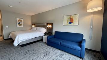 Una habitación de hotel con una cama, un sofá azul, una lámpara de pared y un cuadro.