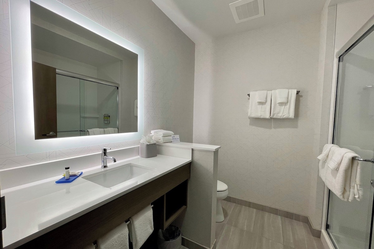 A modern bathroom with a large mirror, a sink, a toilet, and a shower area.