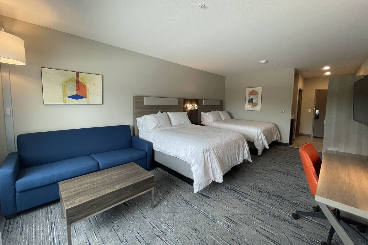 A hotel room with a blue sofa, two single beds, a wooden coffee table, and a desk with a chair.