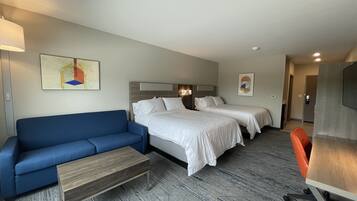 Habitación de hotel con sofá azul, dos camas individuales, una mesita de centro de madera y un escritorio con silla.