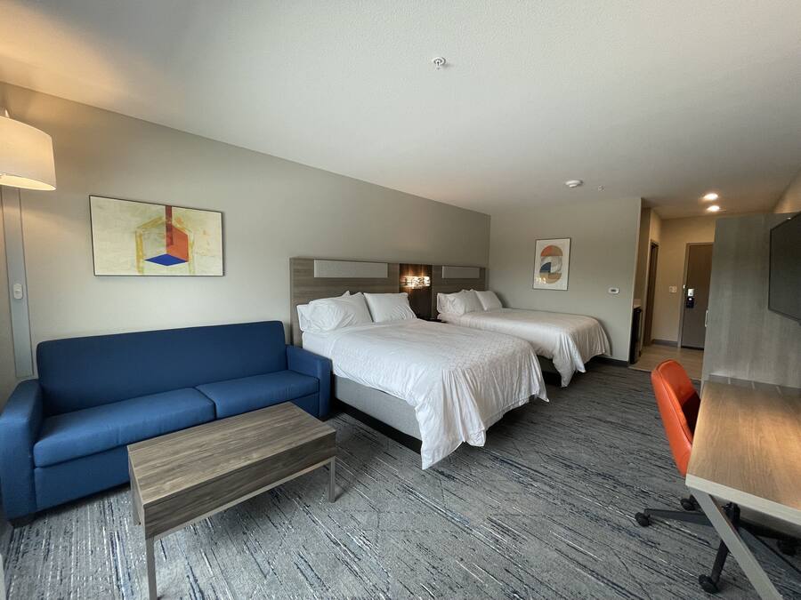 Habitación de hotel con sofá azul, dos camas individuales, una mesita de centro de madera y un escritorio con silla.