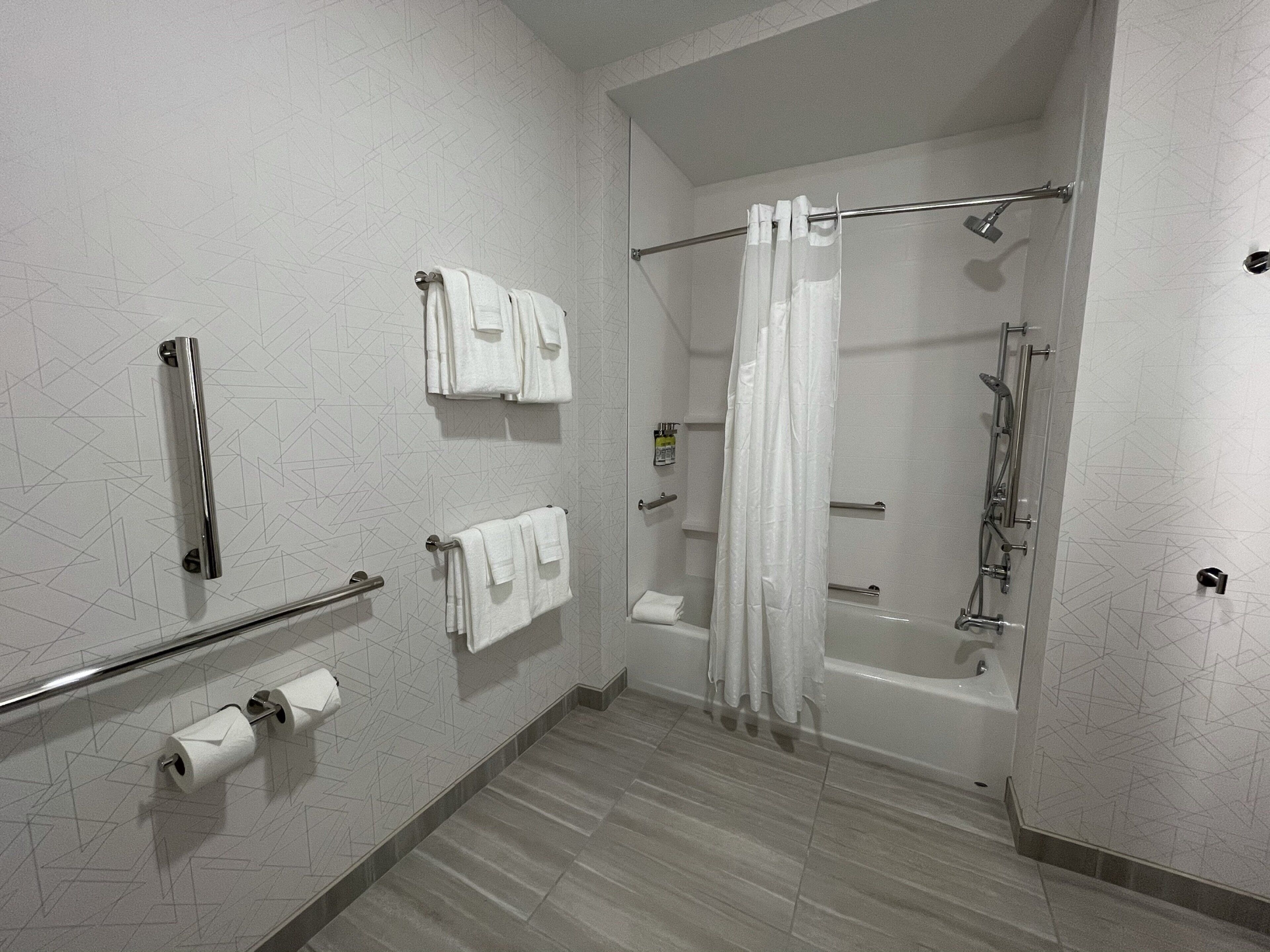 A modern bathroom with a shower, toilet paper, and handrails.