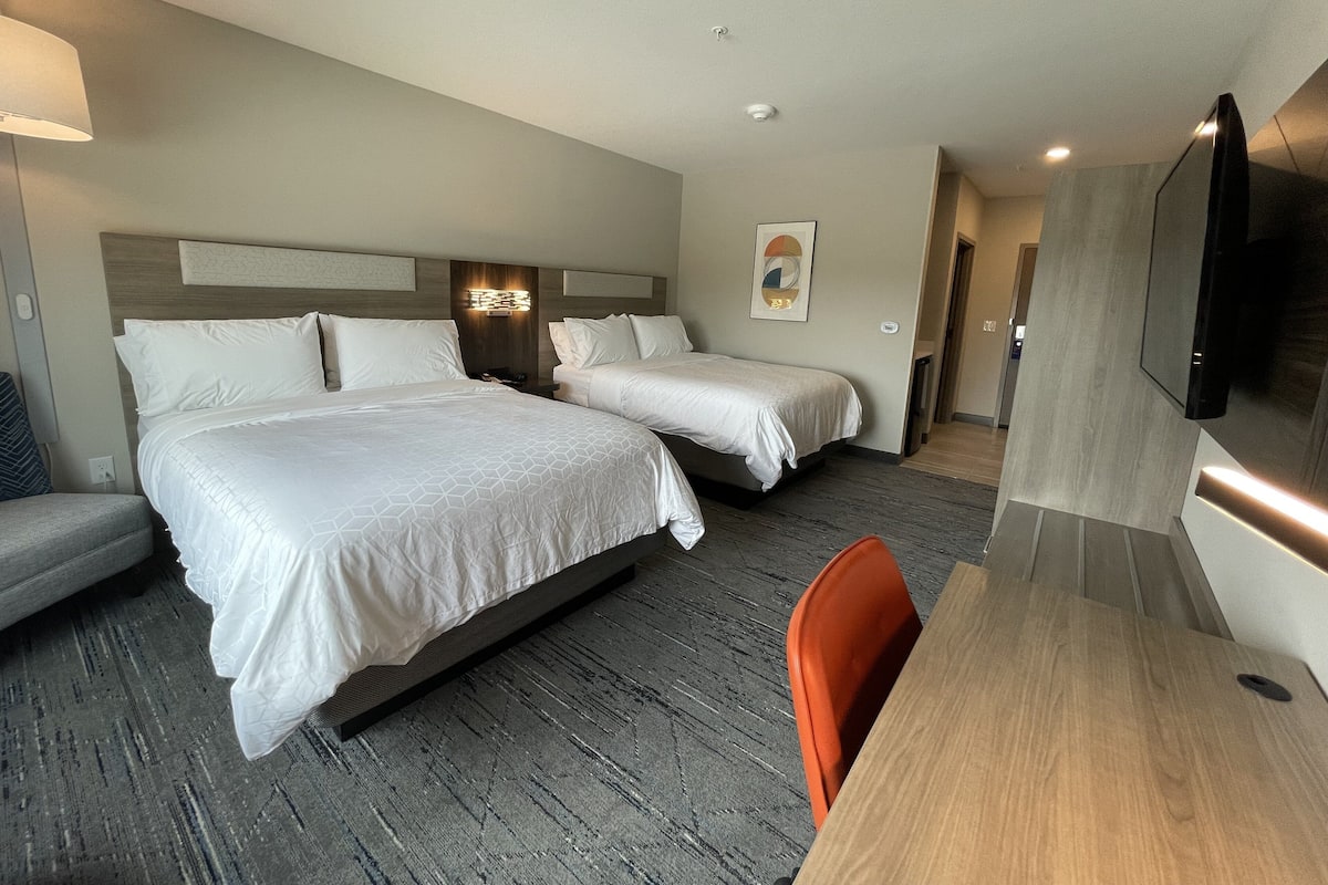 A hotel room with two beds, a desk, a chair, and a TV.