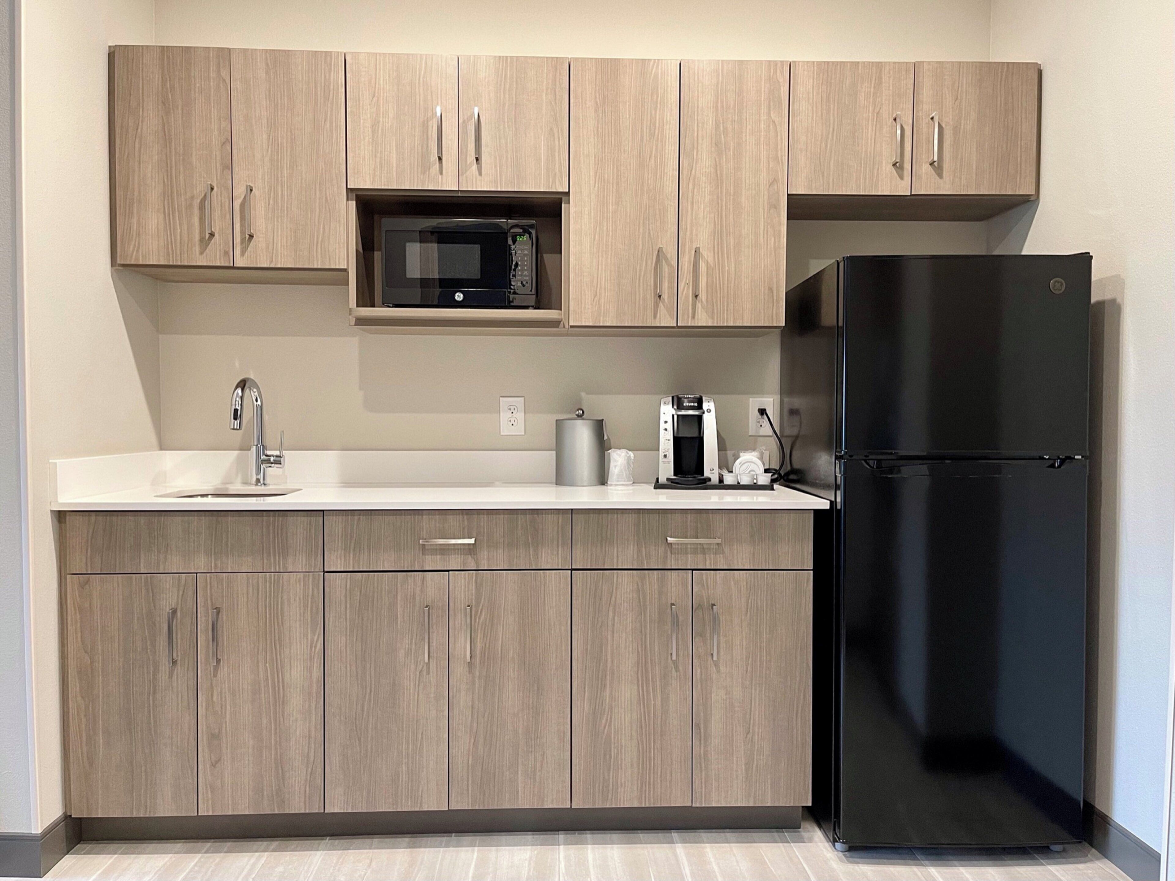 Una cocina con armarios de madera, un refrigerador negro, un microondas, una cafetera y un lavamanos.