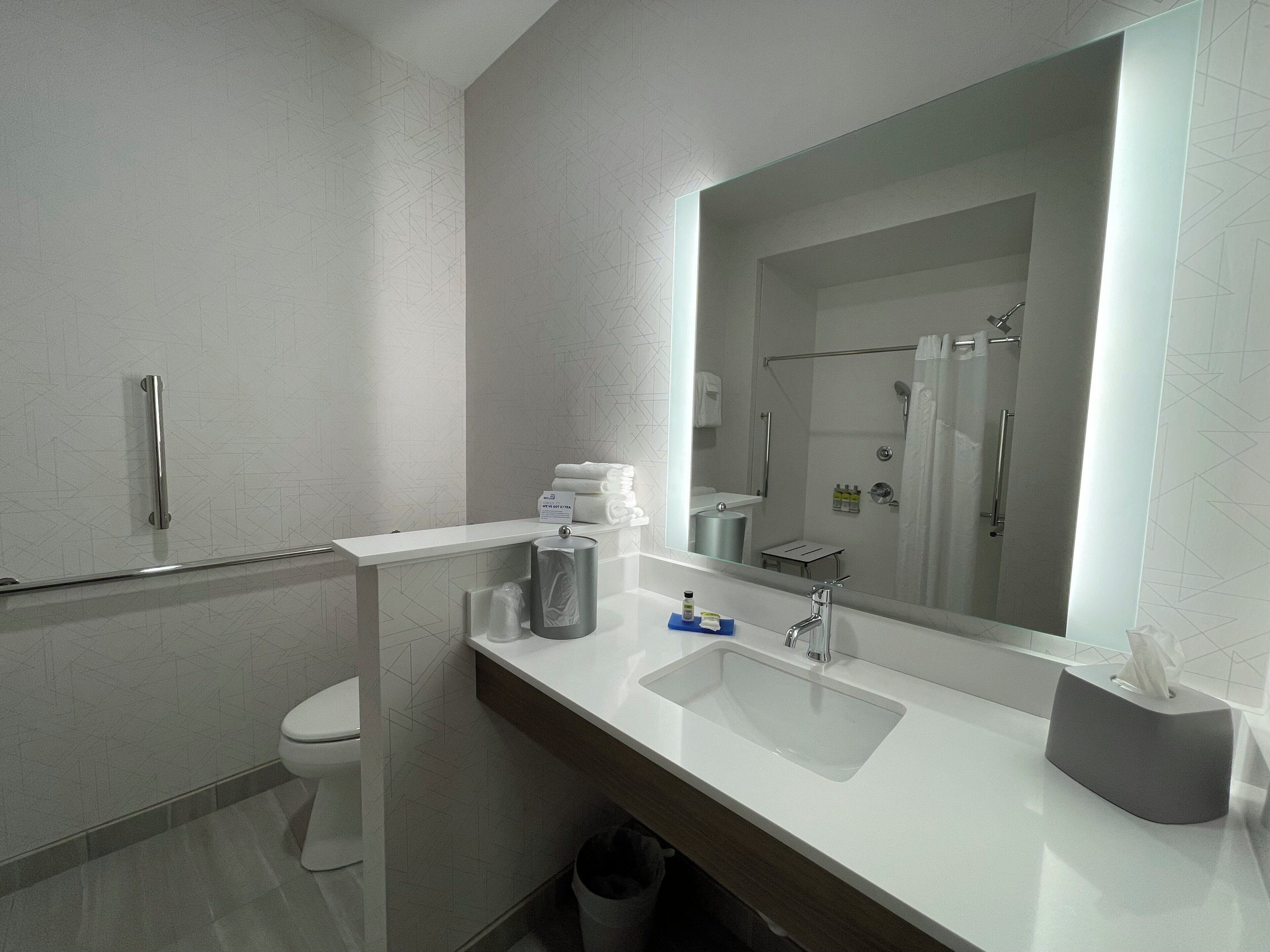 Un baño moderno con un lavabo blanco, un espejo grande y una zona de ducha.
