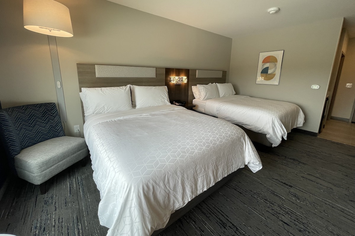 A hotel room with two beds, a sofa, a lamp, and a painting on the wall.
