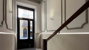 A hallway with a wooden staircase, a black door with glass panels, and a view of a building outside. - Belvedere | The Rentals Collection (San Sebastián/Donostia)