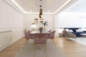 A dining area with a glass table, pink chairs, a hanging light fixture, and a sofa in the background. - Belvedere | The Rentals Collection (San Sebastián/Donostia)