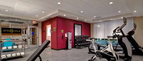 Une salle de sport équipée de matériel d’exercice, un porte-haltères fixé au mur et une porte portant l’inscription « SORTIE ».