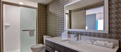 Un baño moderno con cabina de ducha de vidrio, inodoro, tocador con espejo y lavamanos.