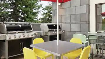 An outdoor patio with a stainless steel grill, yellow chairs, and a red umbrella.
