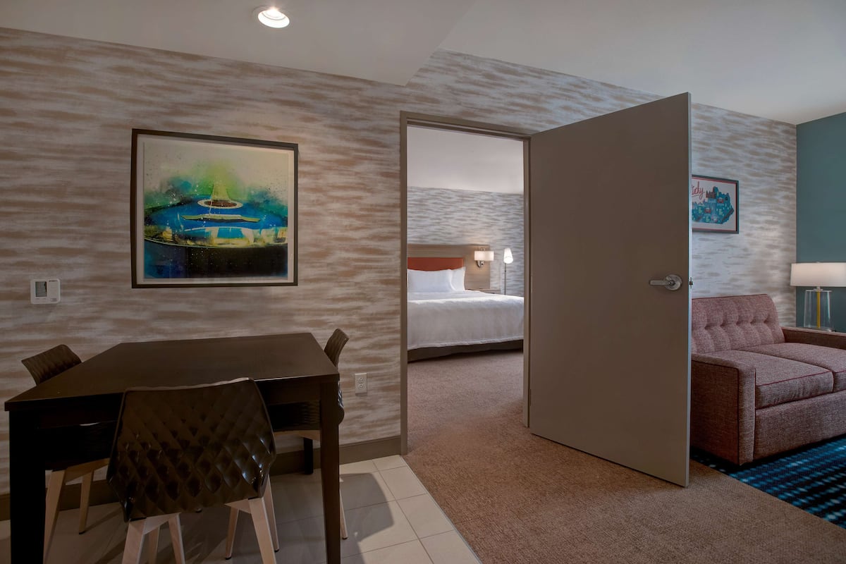 Una habitación de hotel con una mesa de comedor, sillas, una cama, un sofá y un cuadro en la pared.