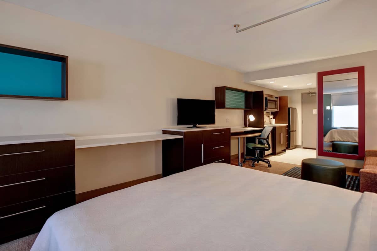 Una habitación de hotel con cama, escritorio, computadora, televisor y espejo.