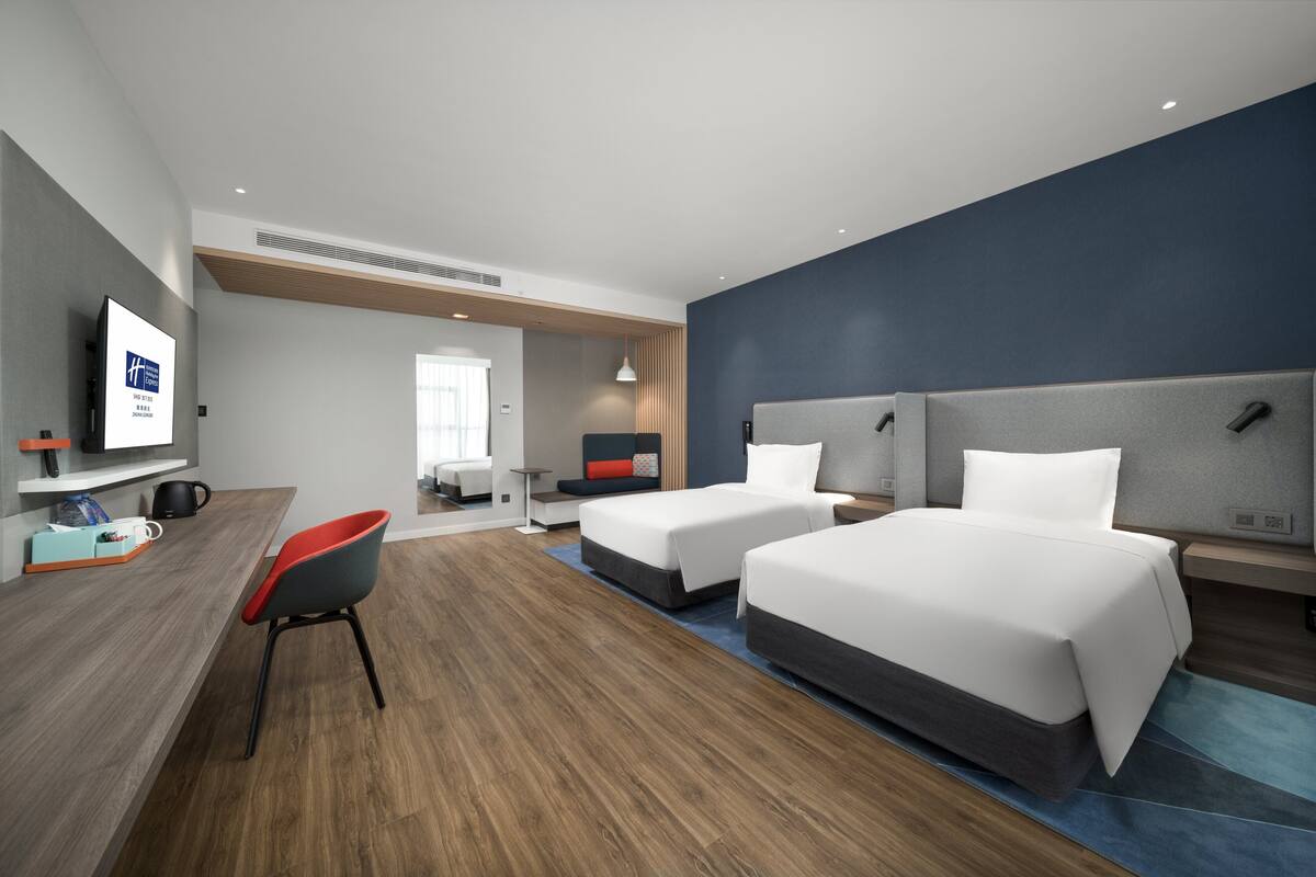 A modern hotel room with two beds, a desk, a chair, and a TV.