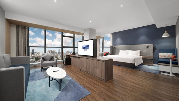 A modern hotel room with a large window, a bed, a desk, and a seating area. - Holiday Inn Express Zhuhai Gongbei by IHG (Zhuhai)