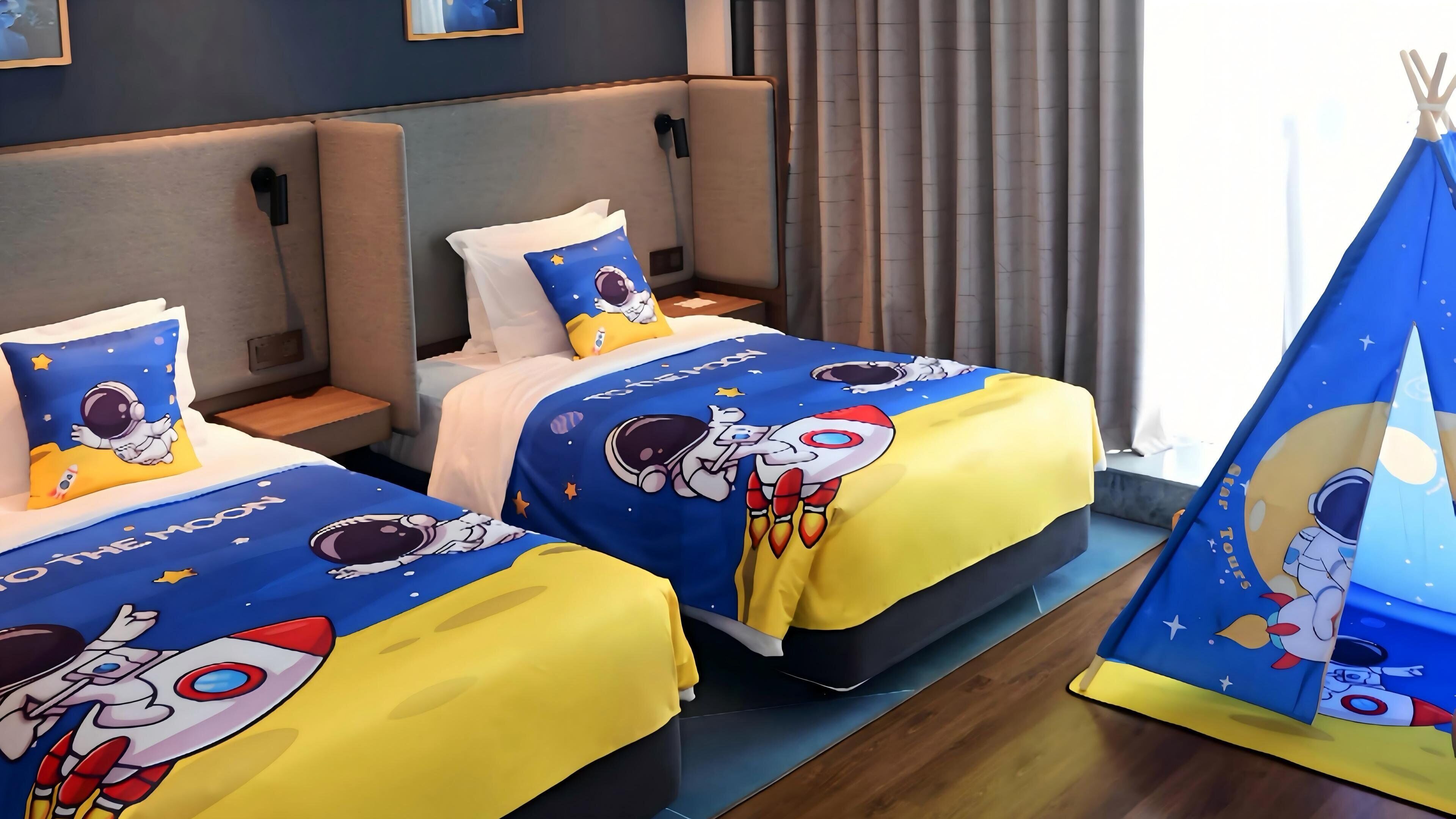 Two adjacent hotel beds with astronaut-themed bedding and a tent-like structure with a space theme.