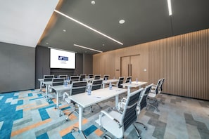 A conference room with a large screen, multiple tables, and chairs. - Holiday Inn Express Zhuhai Gongbei by IHG (Zhuhai)