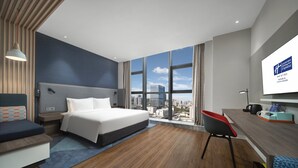 A modern hotel room with a large bed, a desk, a chair, and a city view through large windows. - Holiday Inn Express Zhuhai Gongbei by IHG (Zhuhai)