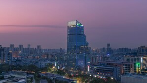 A high-rise hotel with a modern glass facade, surrounded by a dense urban skyline at dusk. - Holiday Inn Express Zhuhai Gongbei by IHG (Zhuhai)
