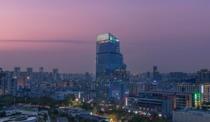 A high-rise hotel with a modern glass facade, surrounded by a dense urban skyline at dusk. - Holiday Inn Express Zhuhai Gongbei by IHG (Zhuhai)