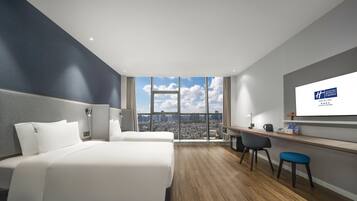 Una habitación de hotel moderna con una cama grande, un escritorio y vistas a un paisaje urbano a través de un ventanal.