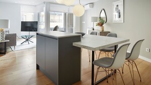 Et moderne køkken med en central ø, et spiseområde med et marmorbord og en opholdsstue med sofa og fjernsyn.