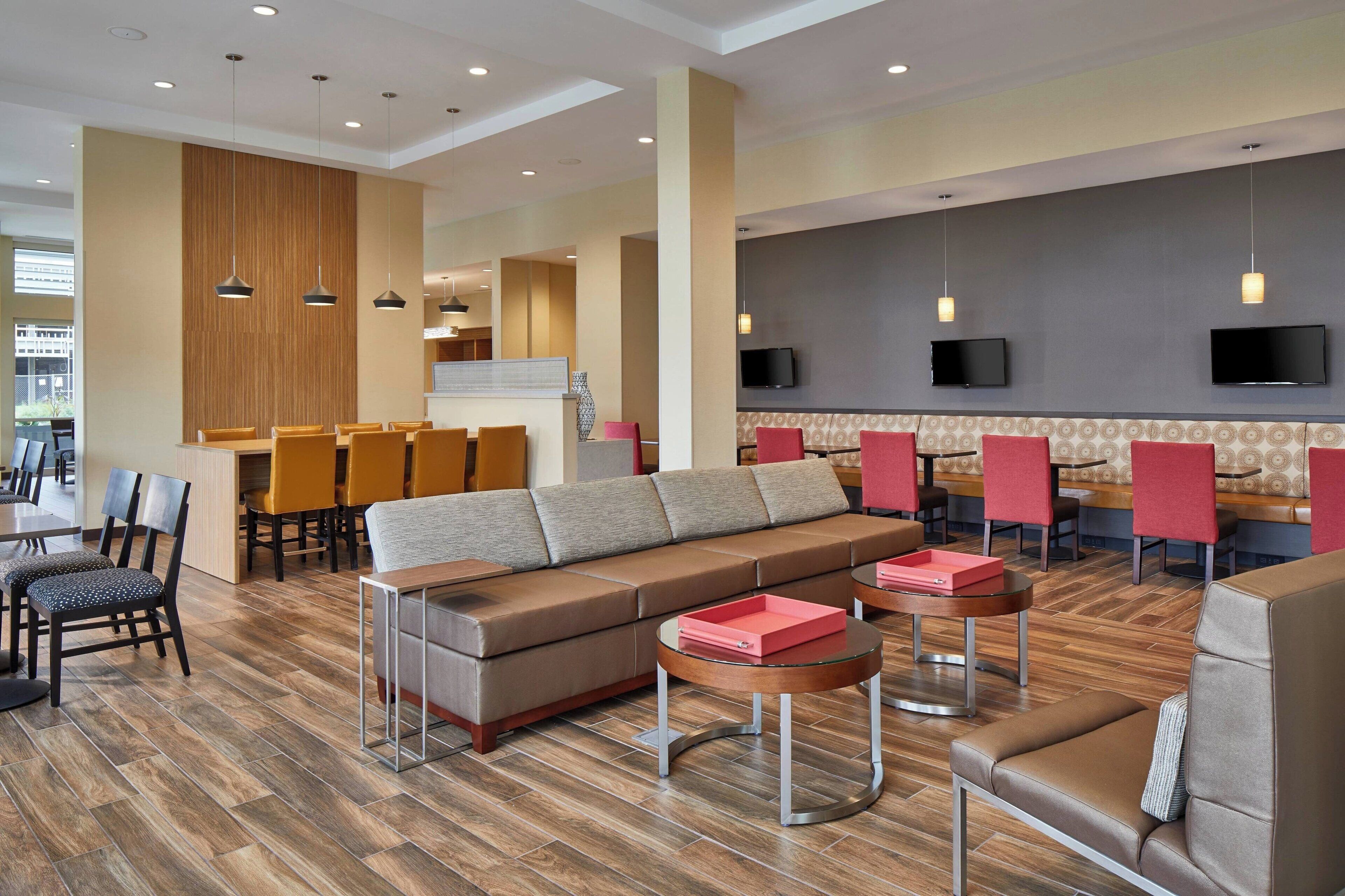 Un moderno vestíbulo de hotel con sofá, zona de comedor y pantallas de televisión.