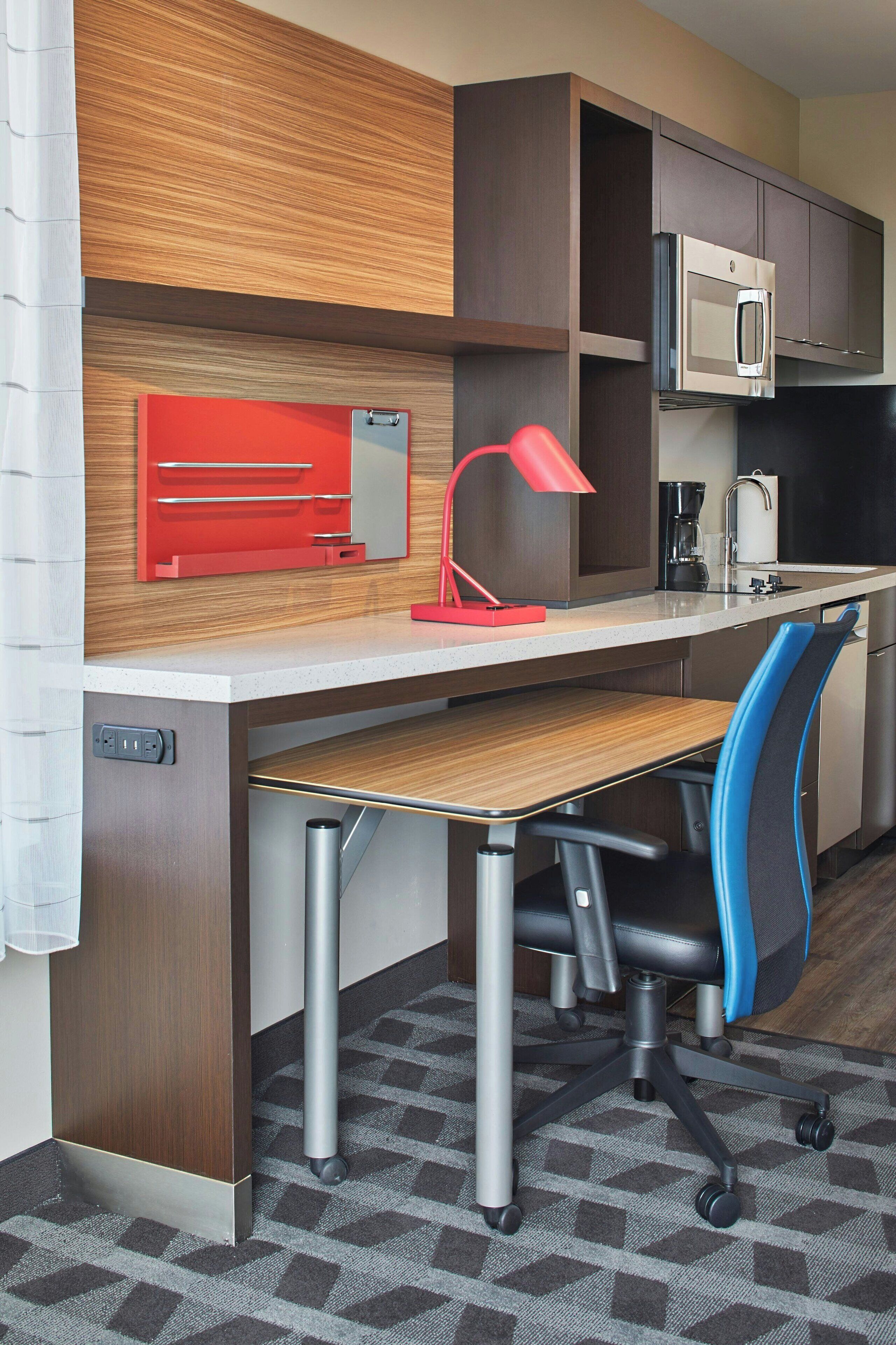 A modern kitchen with a built-in microwave, a red desk lamp, and a blue office chair.