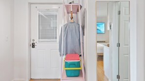 Un pasillo con una puerta blanca, un perchero con una chaqueta y un televisor en la pared.