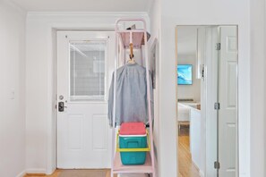 Un corridoio con una porta bianca, un appendiabiti con un cappotto e una televisione appesa al muro.