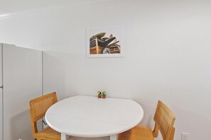 A round white table with two wicker chairs, a framed picture on the wall, and a door to the left.