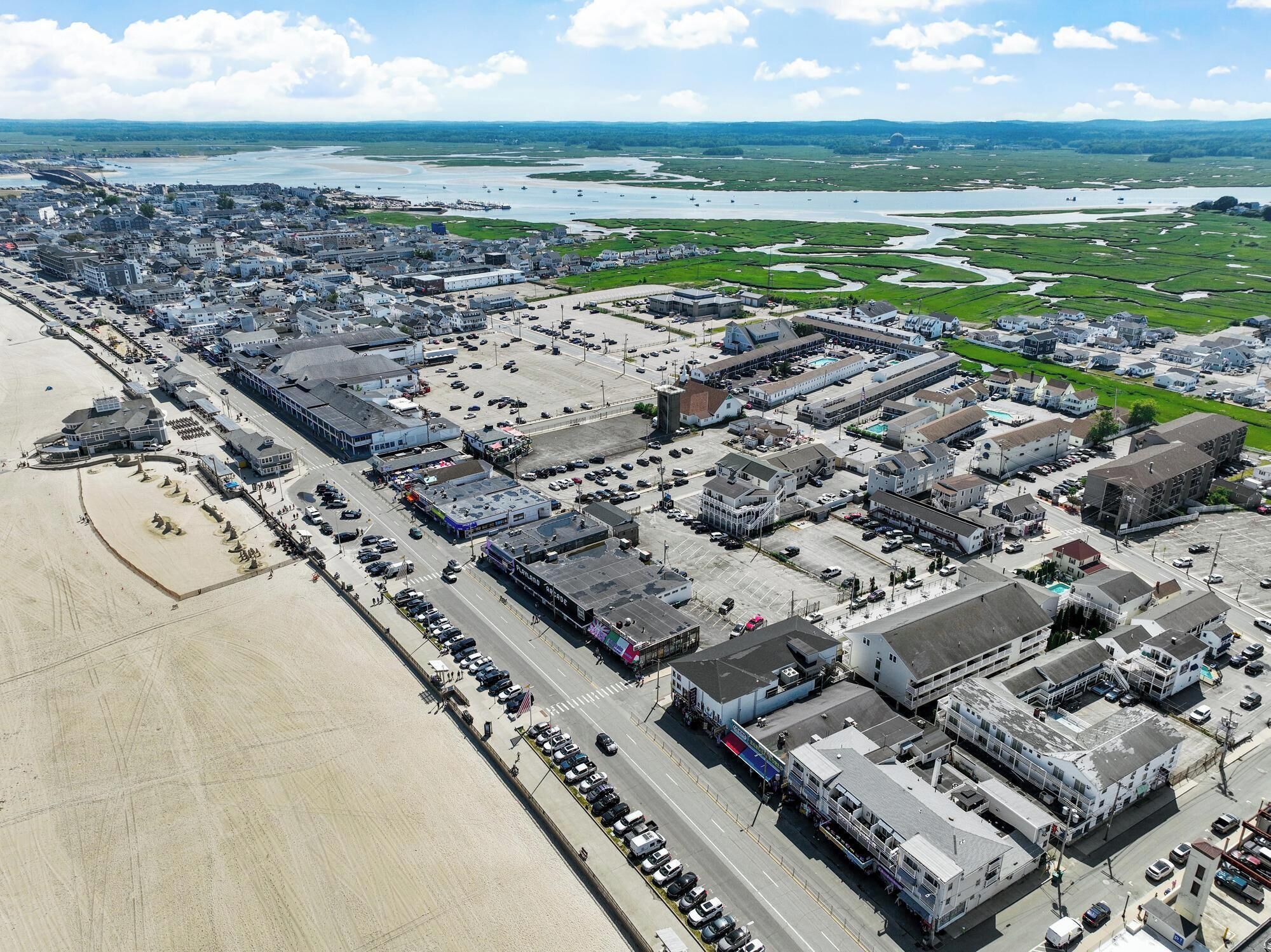 An aerial view of a coastal town with a large parking area, buildings, and a beach.