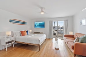 A hotel room with a bed, a sofa, a TV, a ceiling fan, and a view of the city.