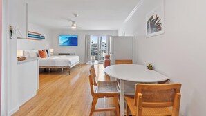 Una habitación de hotel moderna con una cama, una mesa de comedor con sillas, un televisor y vista a la ciudad.