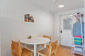 A room with a white door, a white table with four chairs, a small framed picture on the wall, and a rack with folded clothes and a towel.