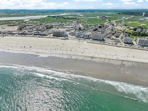 An aerial view of a coastal town with a wide sandy beach, a marina, and a water tower.