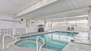 Una piscina interior con agua cristalina, una escalera de piscina y un cartel con las normas de la piscina.