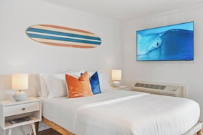 A hotel room with a bed, two bedside tables, a wall-mounted TV, and a surfboard decoration.