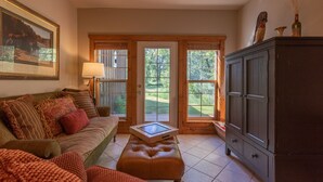 A cozy living room with a sofa, ottoman, and a cabinet. There are large windows with a view of greenery outside. - Luxury on 300 ft of Snake River, Southfork,Hot Tub,Fly Fishing Near Jackson Hole (Irwin)