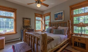A bedroom with a wooden bed, large windows, a ceiling fan, and a painting on the wall. - Luxury on 300 ft of Snake River, Southfork,Hot Tub,Fly Fishing Near Jackson Hole (Irwin)
