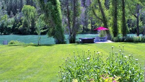 A lush green lawn with a bench and a red umbrella near a lake, surrounded by trees. - Luxury on 300 ft of Snake River, Southfork,Hot Tub,Fly Fishing Near Jackson Hole (Irwin)