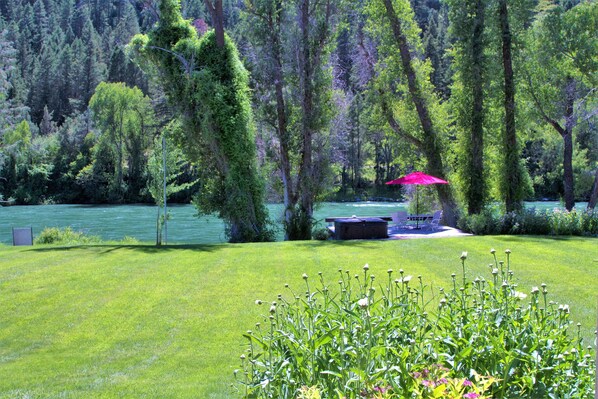 A lush green lawn with a bench and a red umbrella near a lake, surrounded by trees. - Luxury on 300 ft of Snake River, Southfork,Hot Tub,Fly Fishing Near Jackson Hole (Irwin)