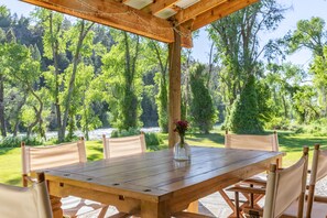 A wooden table with six chairs, a vase with flowers, and a view of a forested area. - Luxury on 300 ft of Snake River, Southfork,Hot Tub,Fly Fishing Near Jackson Hole (Irwin)